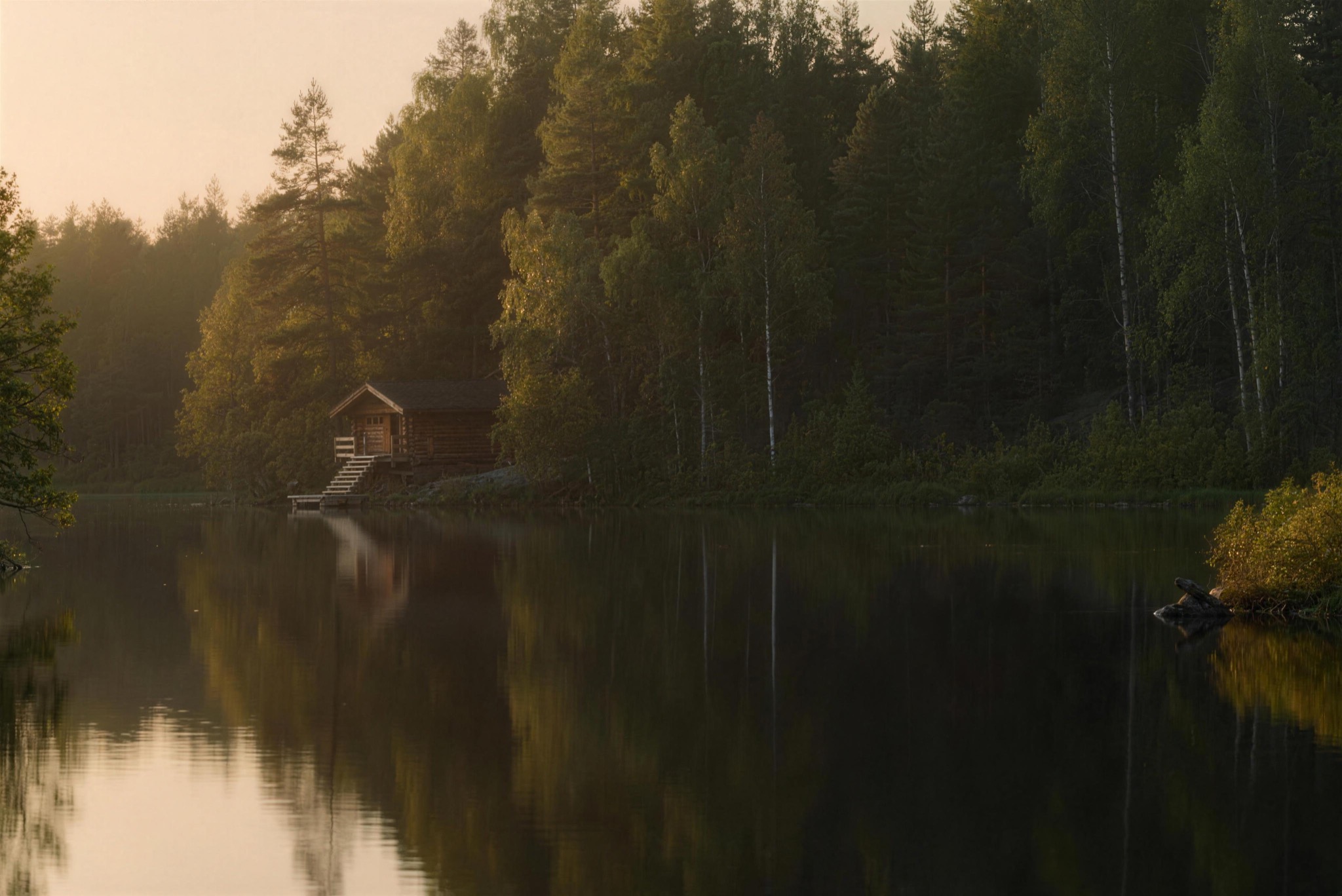 A sauna by a still lake in summer light