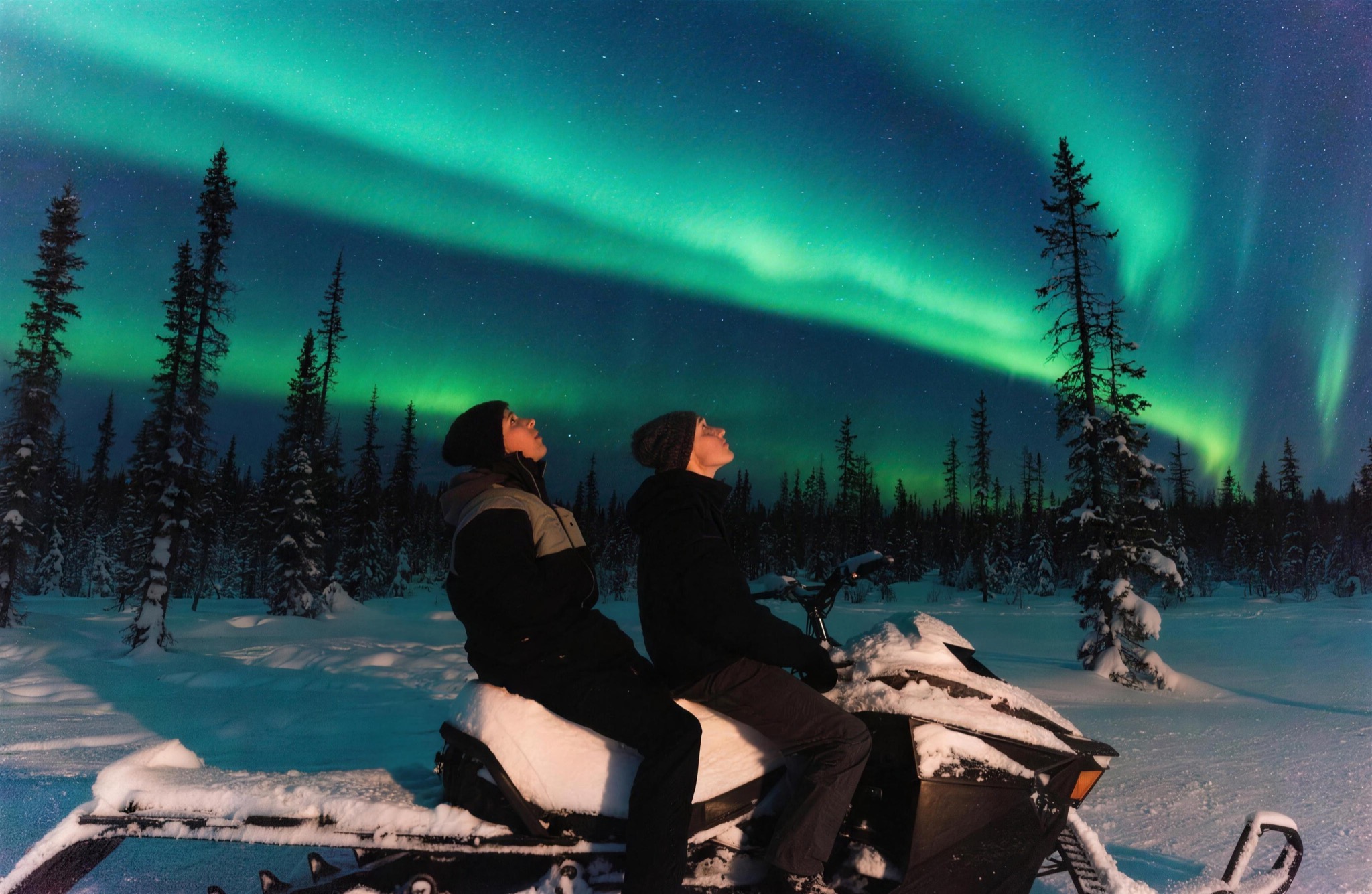 Two guests on a snowmobile under the aurora
